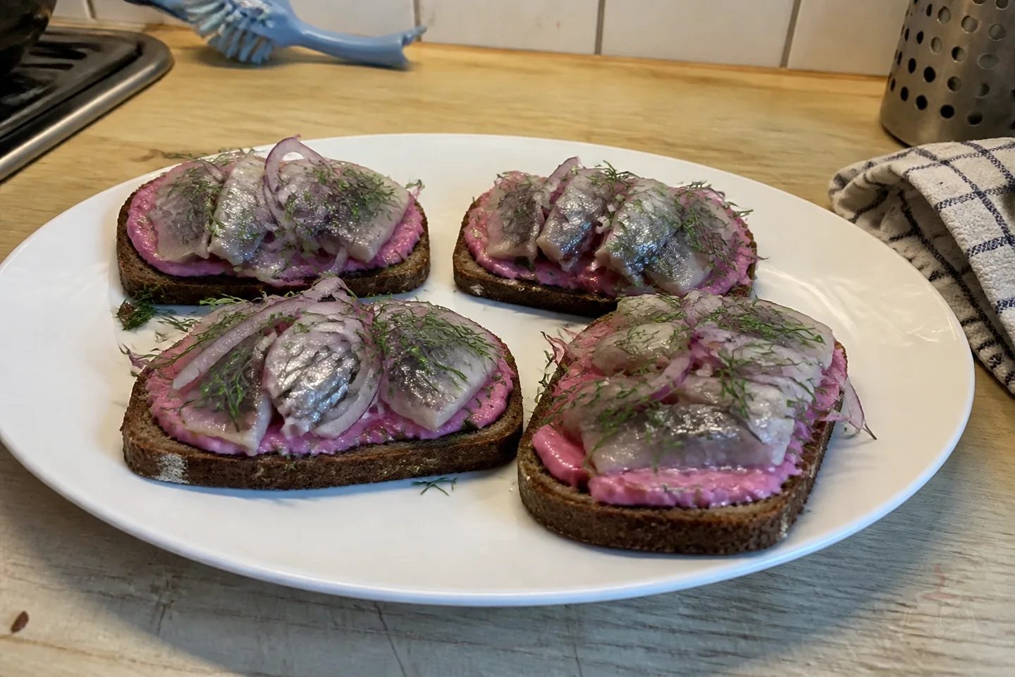 Four rye sandwiches with beet spread, herring, red onion, and dill