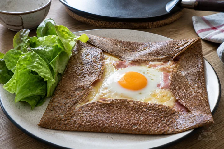 Breton buckwheat galette with ham, melted cheese, egg, and dressed greens