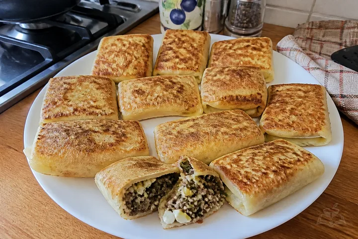 Cornmeal blintzes filled with beef, onions, egg, and parsley on a ceramic plate