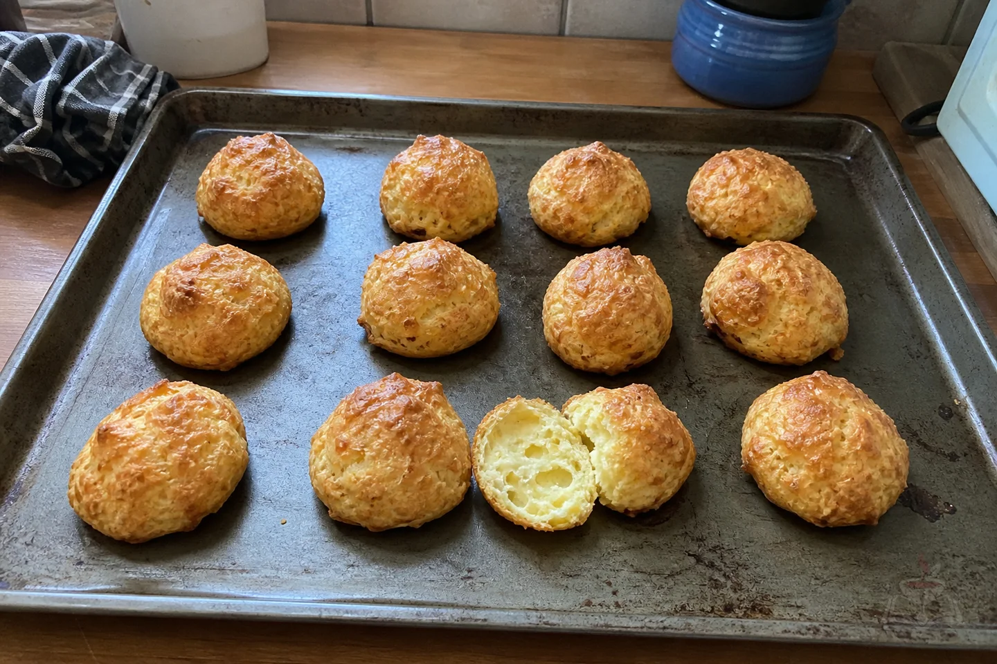 Twelve golden French Gruyère gougères with one broken open