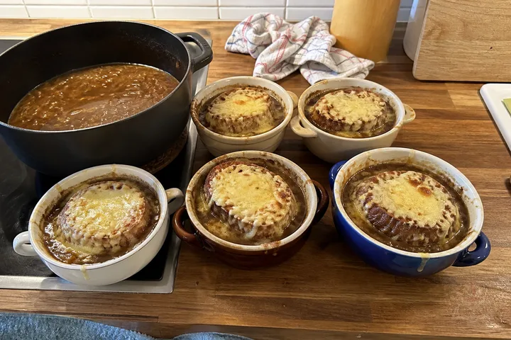 French onion soup in a brown crock with toasted baguette and browned Gruyère