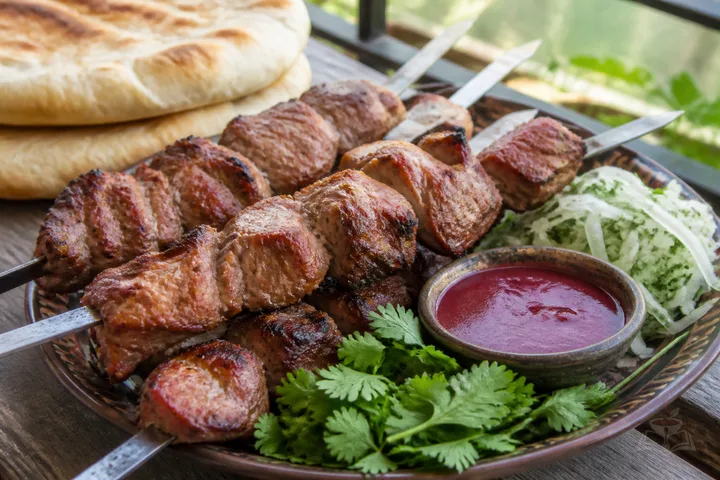 Georgian pork mtsvadi skewers over charcoal with tkemali, onions, and herbs