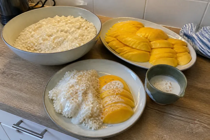 Thai mango sticky rice with two rice mounds, ripe mango, coconut sauce, and sesame