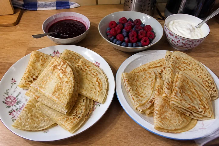 Thin folded blini with sour cream, berry preserve, raspberries, and blueberries